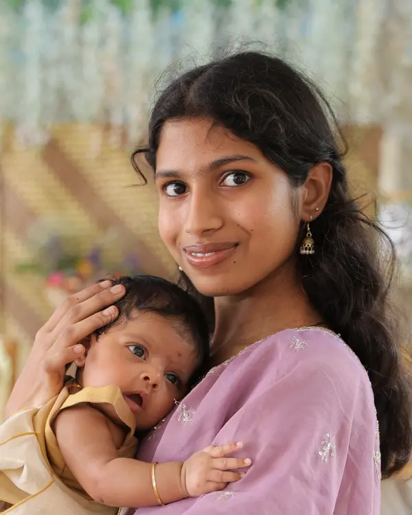 Nirupama S in a lilac sari, smiling and holding a baby