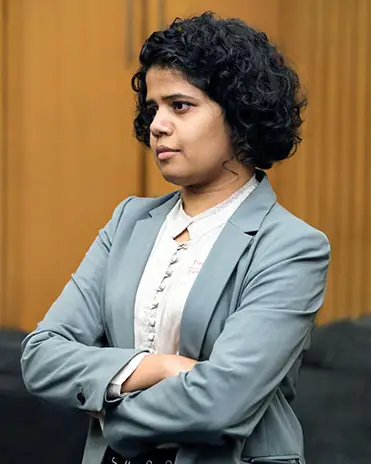 Siya R in a grey blazer with arms folded, looking to the side